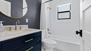 A modern bathroom with a white bathtub, a white toilet, and a vanity with a gold faucet. - Casa Sunshine NEW (West Palm Beach)