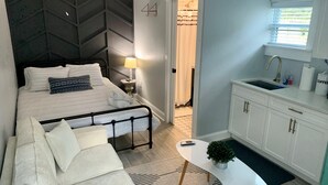 A modern bedroom with a bed, bedside table, lamp, and a view of the bathroom. - Casa Sunshine NEW (West Palm Beach)
