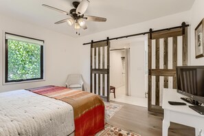 Una camera da letto con un letto, una scrivania, una TV, una ventola a soffitto e una porta scorrevole che dà su un bagno.
