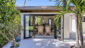 A modern house with a glass door leading to a dining area with wicker furniture. - Cortez Bungalow, 3 Bd 2 Ba, Private Pool (West Palm Beach)