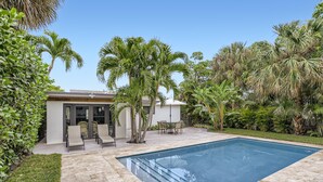 A swimming pool with a patio area, surrounded by palm trees and a building with a glass door. - Cortez Bungalow, 3 Bd 2 Ba, Private Pool (West Palm Beach)