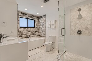 A modern bathroom with a bathtub, toilet, and glass-enclosed shower.