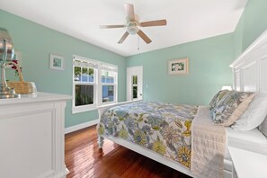 A bedroom with a bed, a ceiling fan, a dresser, and framed pictures on the walls.