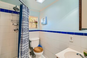 Enjoy a refreshing shower with a view of palm trees from the window, a bathtub, and a sink with a mirror.