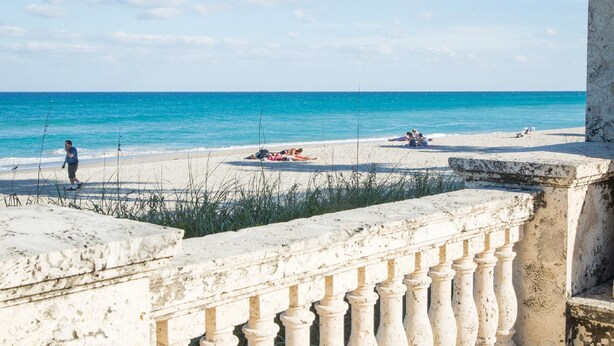 A beach with a stone balustrade, clear blue water, and people relaxing on the sand. - Key Lime Bungalow 2 BD 1 BA With Private Pool (West Palm Beach)