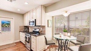 A modern kitchen with white cabinets, a gas stove, and a microwave. There's a dining area with a glass table and chairs. - Key Lime Bungalow 2 BD 1 BA With Private Pool (West Palm Beach)