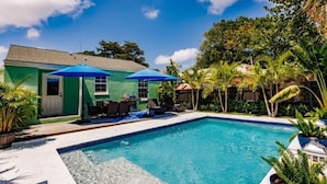 A swimming pool with a green house and blue umbrellas in the background. - Key Lime Bungalow 2 BD 1 BA With Private Pool (West Palm Beach)