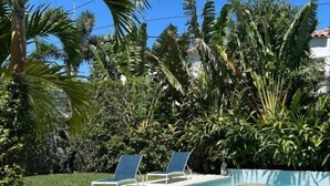A swimming pool with lounge chairs, surrounded by lush greenery and palm trees.
