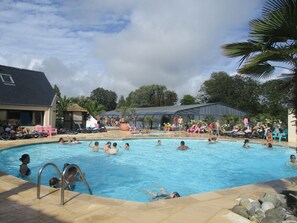 Ein Schwimmbecken mit mehreren Personen im Wasser, umgeben von Liegestühlen und einem überdachten Bereich.