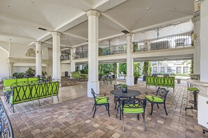 A spacious indoor patio with multiple seating areas, including green cushioned sofas and chairs, and a central round table.