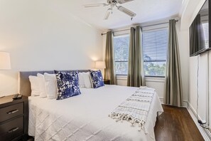 A bedroom with a bed, a nightstand, a lamp, a ceiling fan, and a TV.