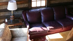 A log cabin interior with a leather sofa, a chandelier made of antlers, and a window with a grid pattern. - Cabin on Pond and Vineyard next to Aging Cave (Chapel Hill)