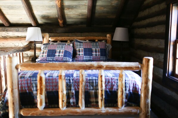 A rustic wooden bed with plaid bedding and two bedside lamps in a log cabin room.
