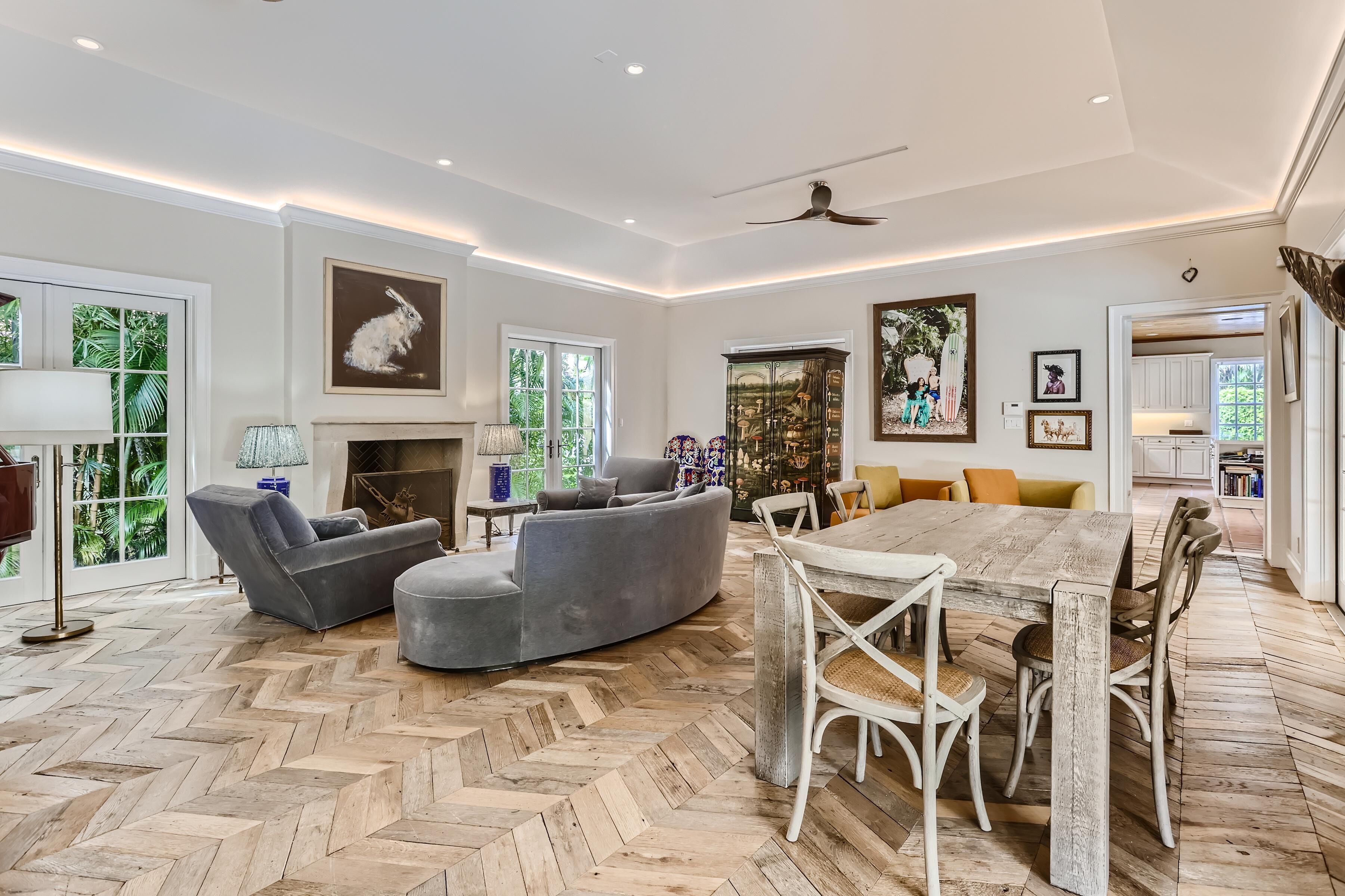 A spacious living room with a herringbone wood floor, a large wooden dining table, and grey sofas.