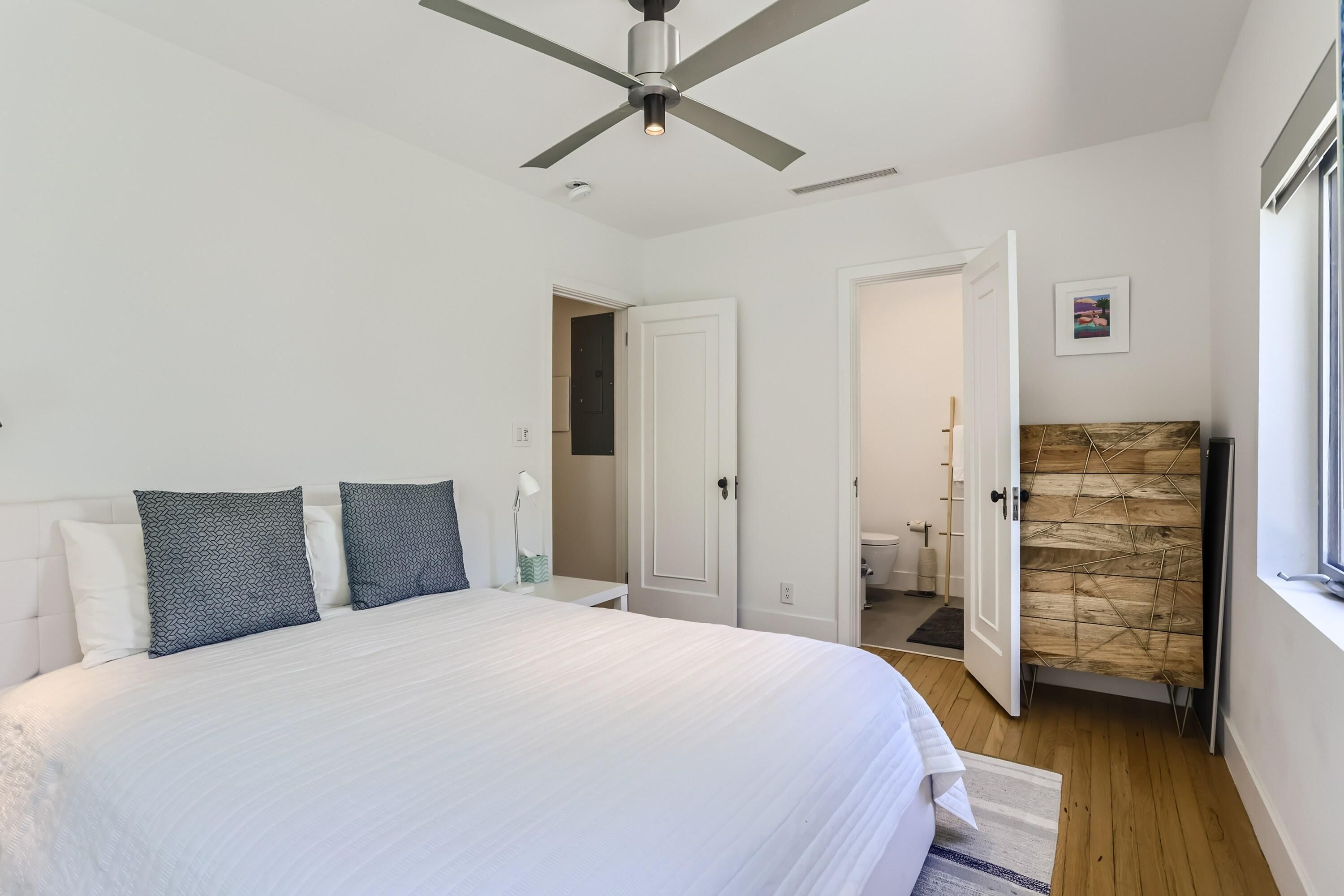 Un dormitorio con una cama grande, un ventilador de techo y vistas al baño.