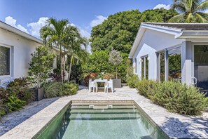 Una casa moderna con piscina, esterno bianco e vegetazione lussureggiante.