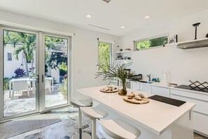 Una cucina moderna con isola centrale, mobili bianchi e una porta scorrevole in vetro che dà su un patio con mobili da esterno.