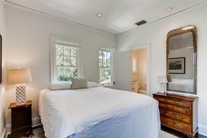 Een slaapkamer met een groot bed, twee ramen, een dressoir en een spiegel.