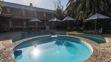 Una piscina con borde de guijarros, rodeada de sillones de descanso y sombrillas.