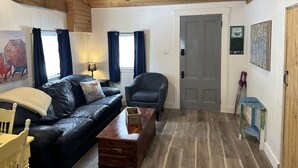 En hyggelig stue med træloft, en sort lædersofa, et træbord og en grå lænestol.