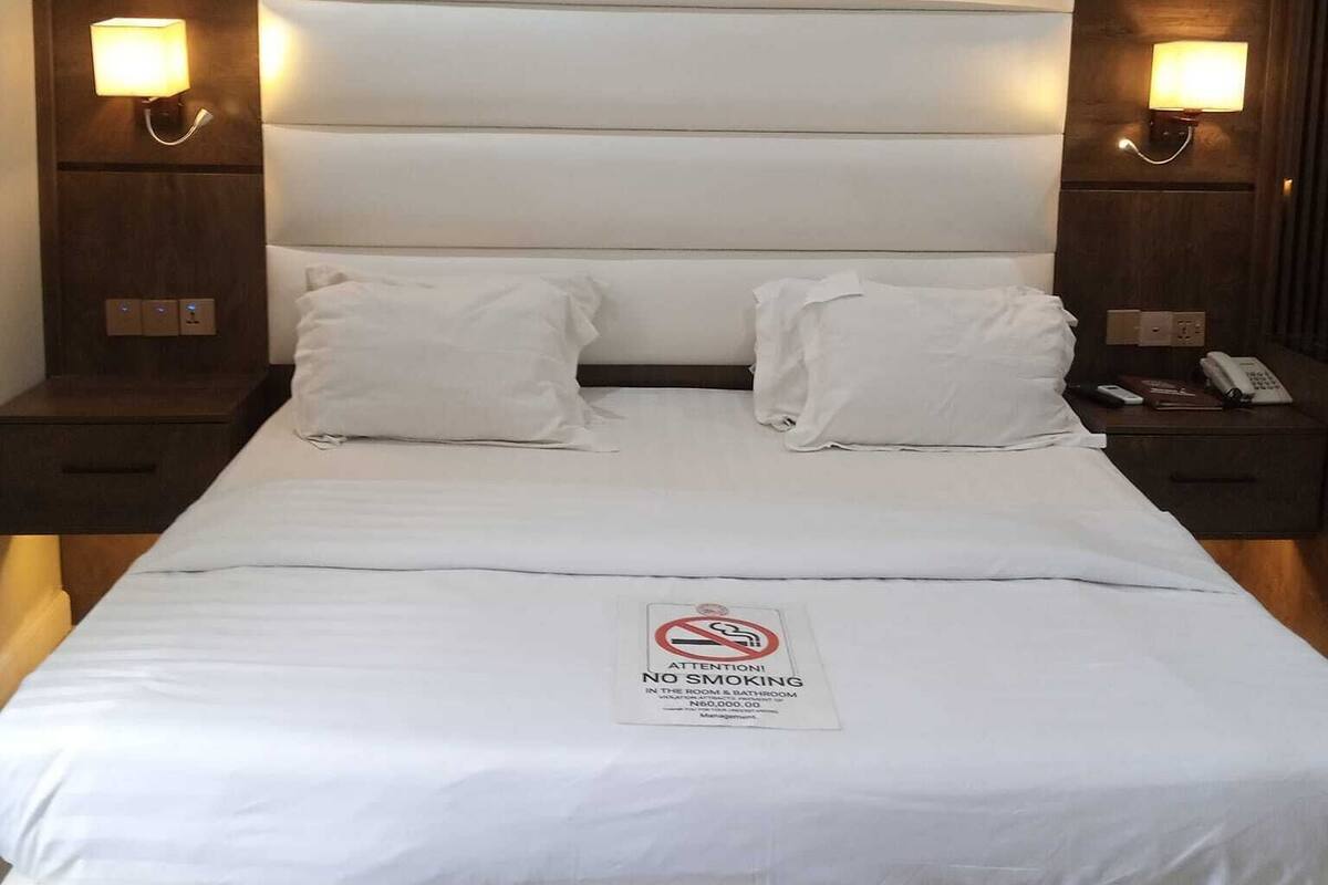 Une chambre d’hôtel avec un grand lit, deux tables de chevet et un panneau «interdiction de fumer» placé sur le lit.