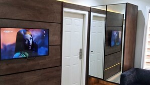 Un salon moderne avec un téléviseur à écran plat fixé sur un mur recouvert de panneaux en bois, une armoire à miroir, un canapé foncé et une petite table basse ronde.