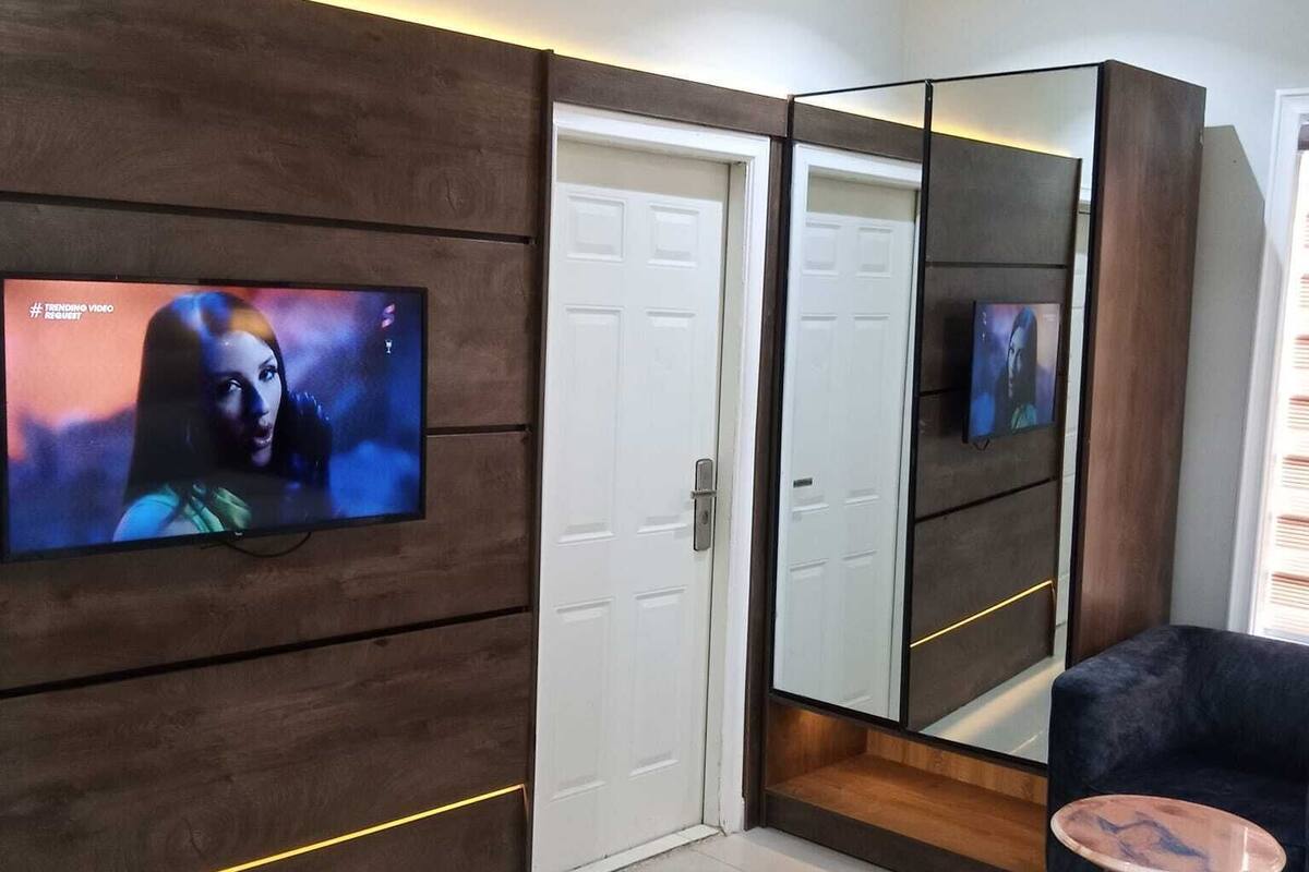 Un salon moderne avec un téléviseur à écran plat fixé sur un mur recouvert de panneaux en bois, une armoire à miroir, un canapé foncé et une petite table basse ronde.