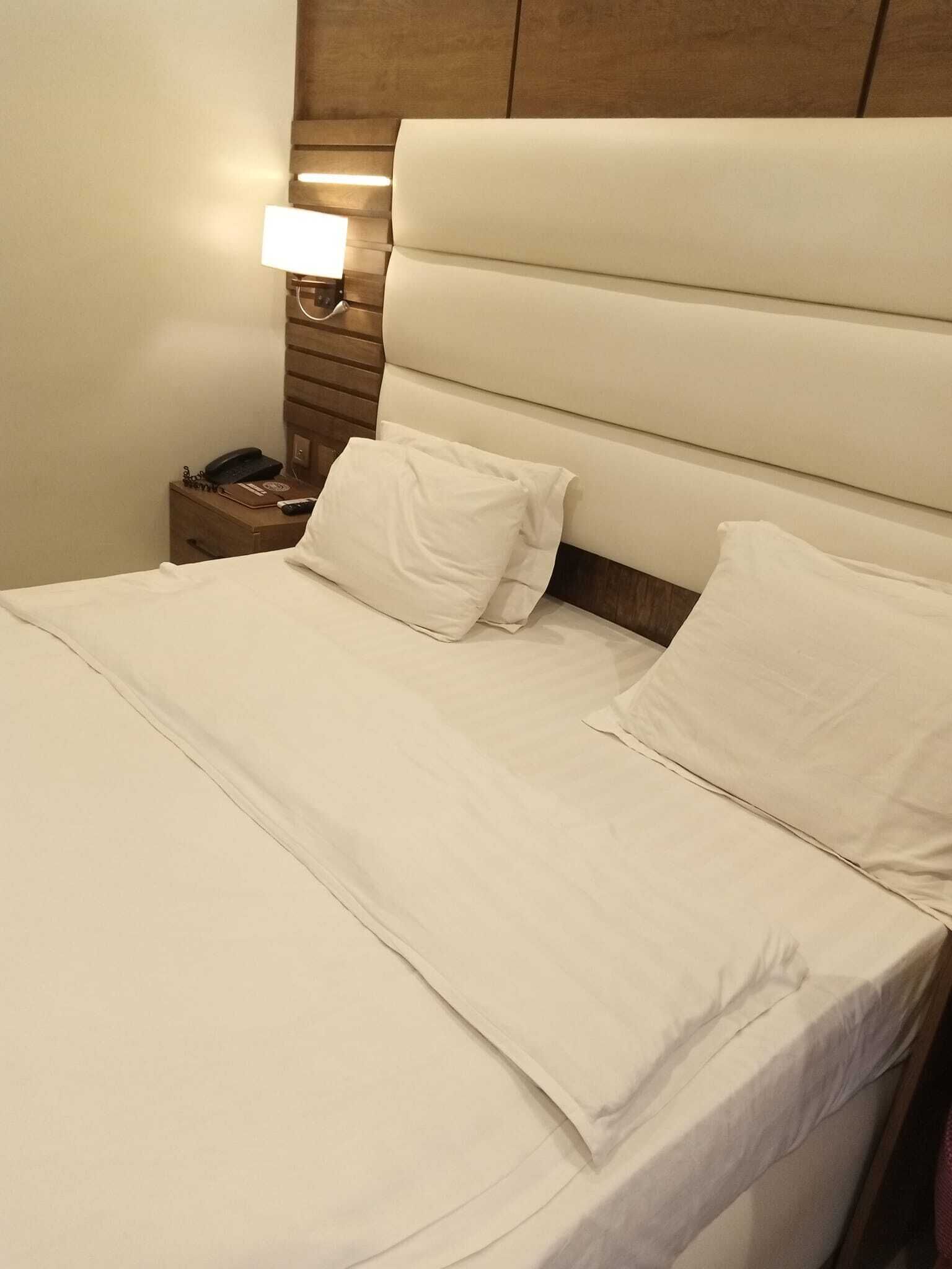 A neatly made bed with white linens, a bedside lamp, and a wooden nightstand with a phone.