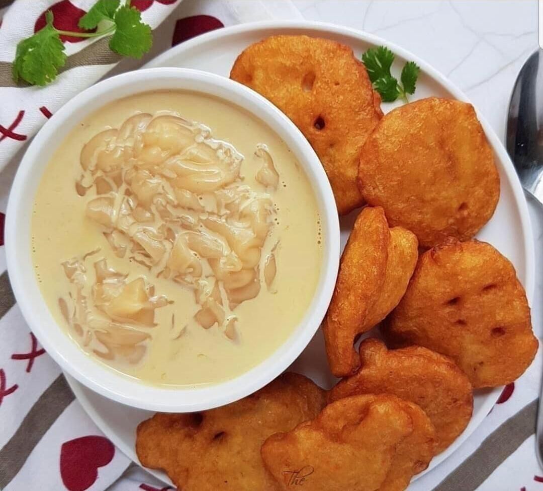 A bowl of soup with a creamy texture, accompanied by several round, golden-brown fried items on a plate.
