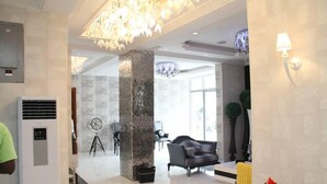 Una hall moderna con un'imponente colonna, un lampadario e un'area relax con divano e poltrone.