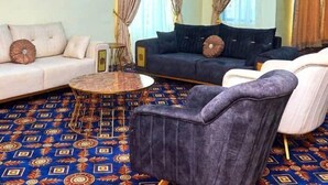 Un soggiorno con divano, poltrona e tavolino, caratterizzato da un tappeto e tende a motivi decorativi.