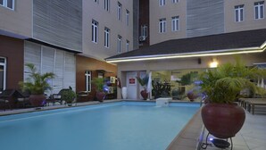 Una piscina con lettini e piante in vaso, circondata da un edificio con numerose finestre e una palestra.