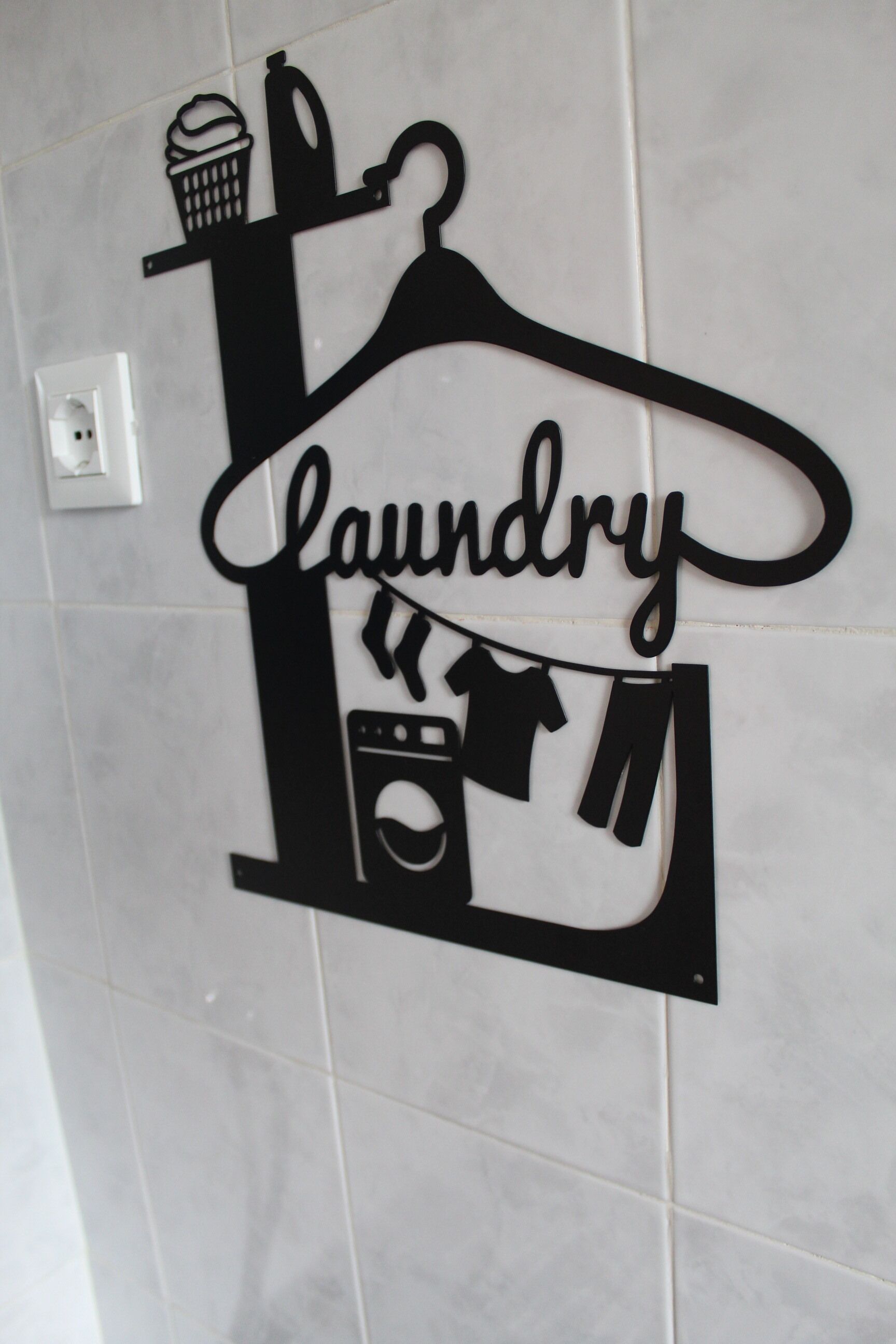 A wall-mounted metal sign with the word "laundry" and icons of a washing machine, clothes, and a bottle.