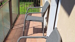 A balcony with two wicker chairs and a metal railing.
