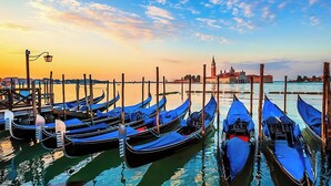 Gondolas docked at a pier with a historic building in the background.