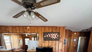 Un soggiorno con rivestimento in legno, ventilatore a soffitto, divano a righe, tavolino in legno e televisore su un mobile.
