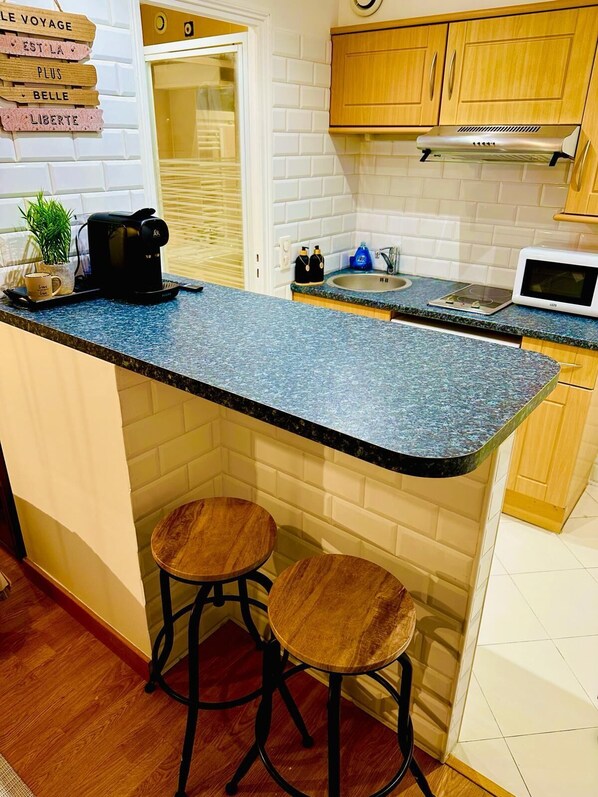 Een keuken met een granieten aanrecht, houten krukken, een koffiezetapparaat, een waterkoker, een magnetron en een roestvrijstalen afzuigkap.