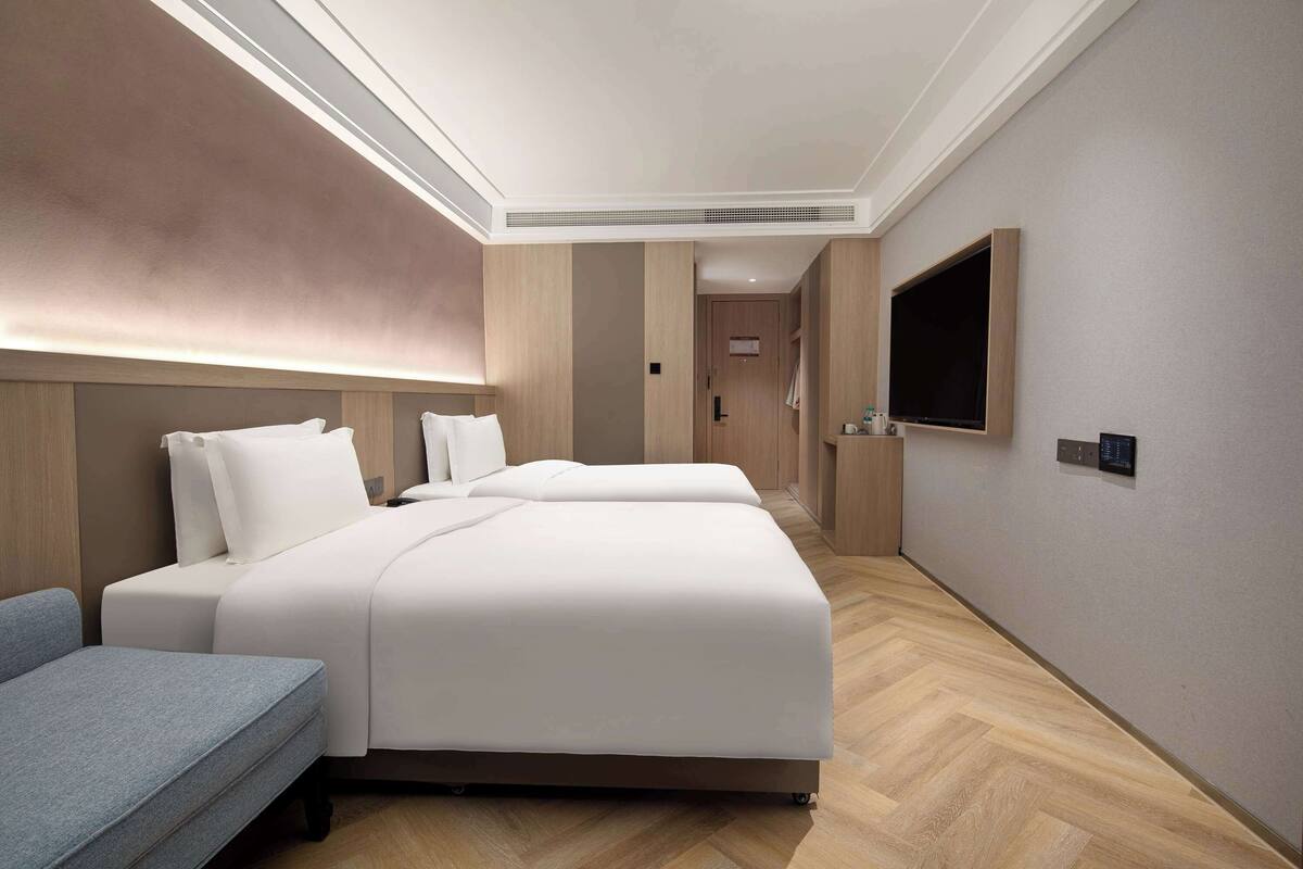 A modern hotel room with a large bed, a sofa, a TV, and a wooden floor.