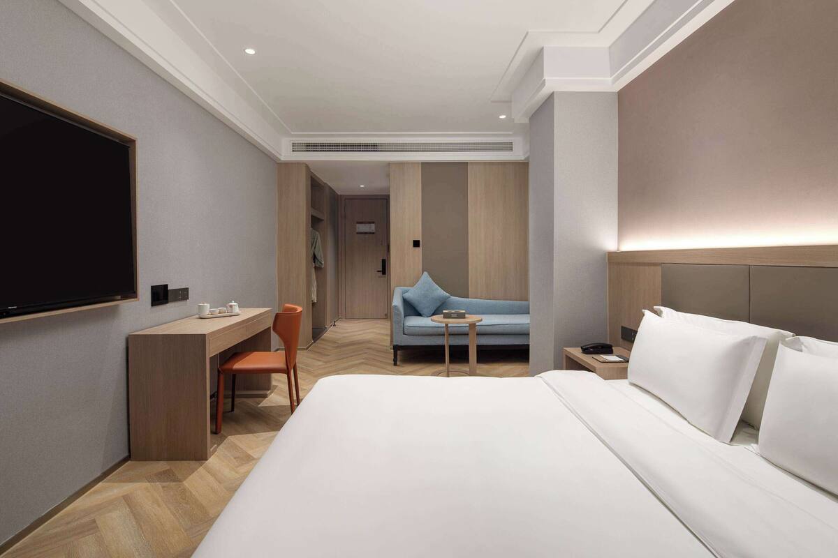 A hotel room with a large bed, a desk, a chair, a sofa, and a TV.