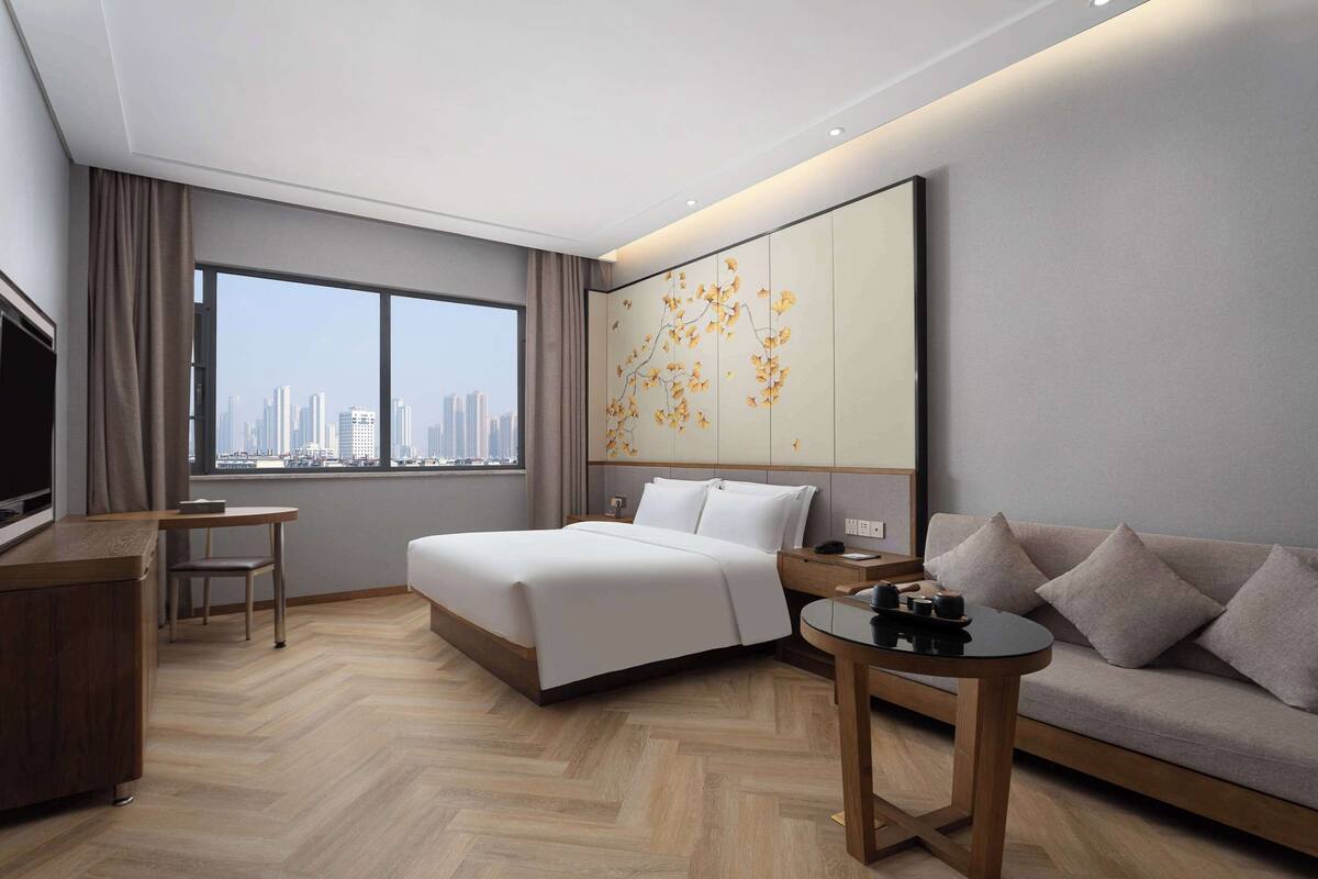 A modern hotel room with a large bed, a sofa, a desk, and a TV.