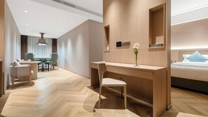 Et moderne hotelværelse med skrivebord i træ, en komfortabel stol, en seng og et lille bord med stole.