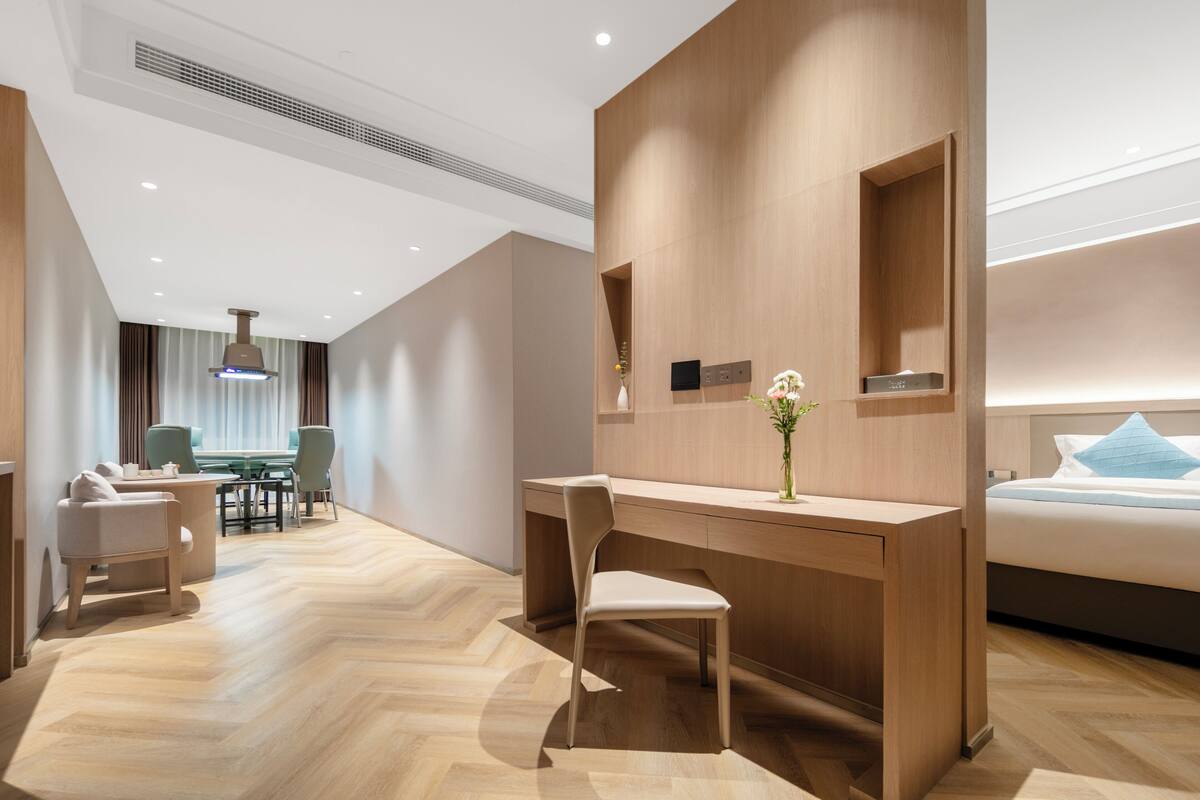 A modern hotel room with a wooden desk, a comfortable chair, a bed, and a small table with chairs.