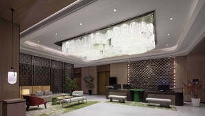 Een moderne lobby met een grote kroonluchter, zithoeken, een receptiebalie en een decoratieve wand.