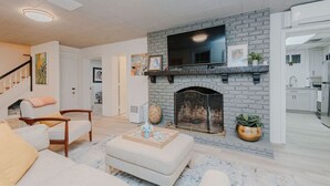 A living room with a fireplace, a sofa, a coffee table, and a TV mounted above the fireplace.