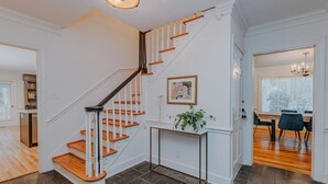 A staircase with wooden steps and white railings, a dining area with a table and chairs, and a potted plant on a console table.