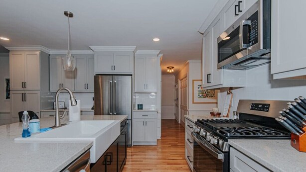 A modern kitchen with stainless steel appliances, white cabinetry, and a wooden floor.