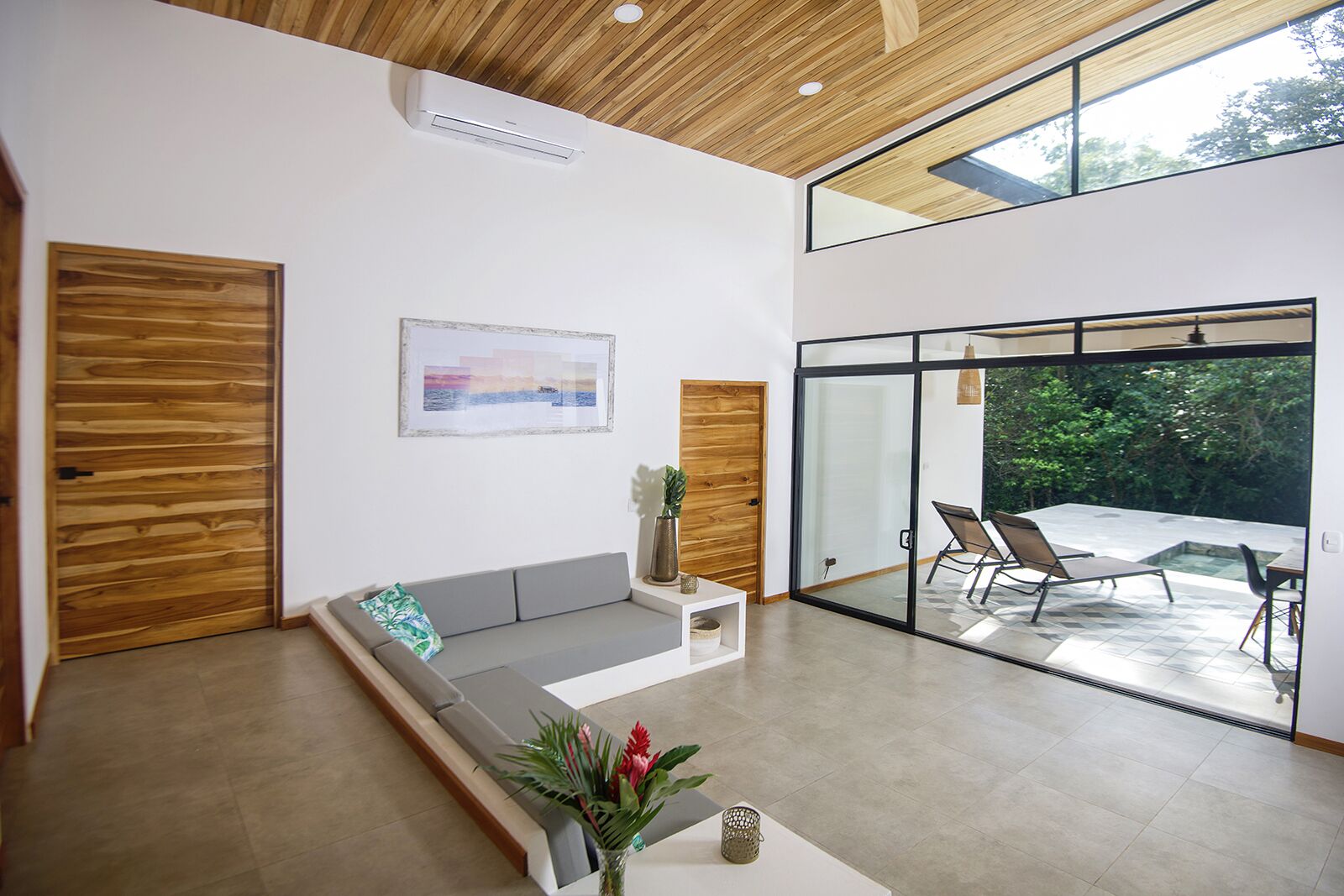 Sala moderna com sofá, mesa de centro e porta de vidro que dá para um pátio externo com piscina e cadeiras.