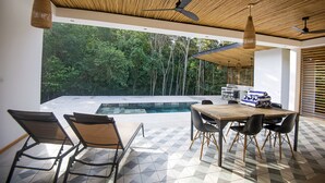 Un área de comedor al aire libre con piscina, sillas y una parrilla.
