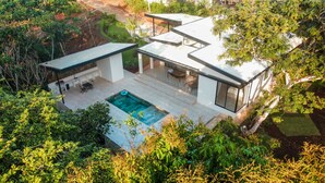 Una casa moderna con piscina, mobiliario de exterior y exuberante vegetación.