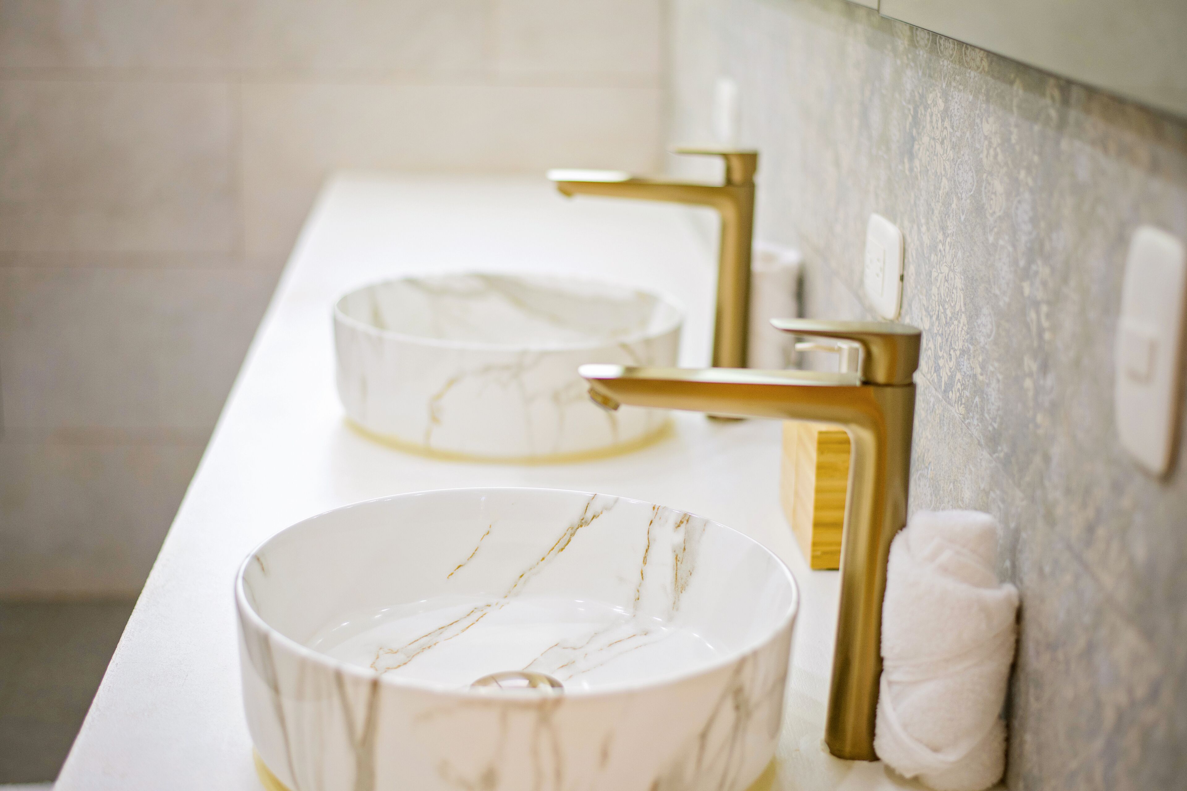A bathroom with two sinks, one with a marble basin and gold faucets, and a towel hanging on the wall.